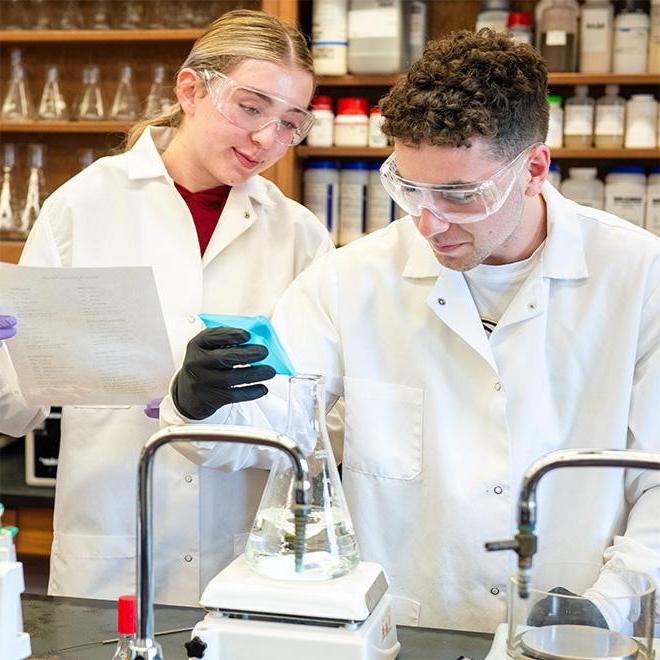 Students dropping chemicals into a beaker as part of a chemical experiment.